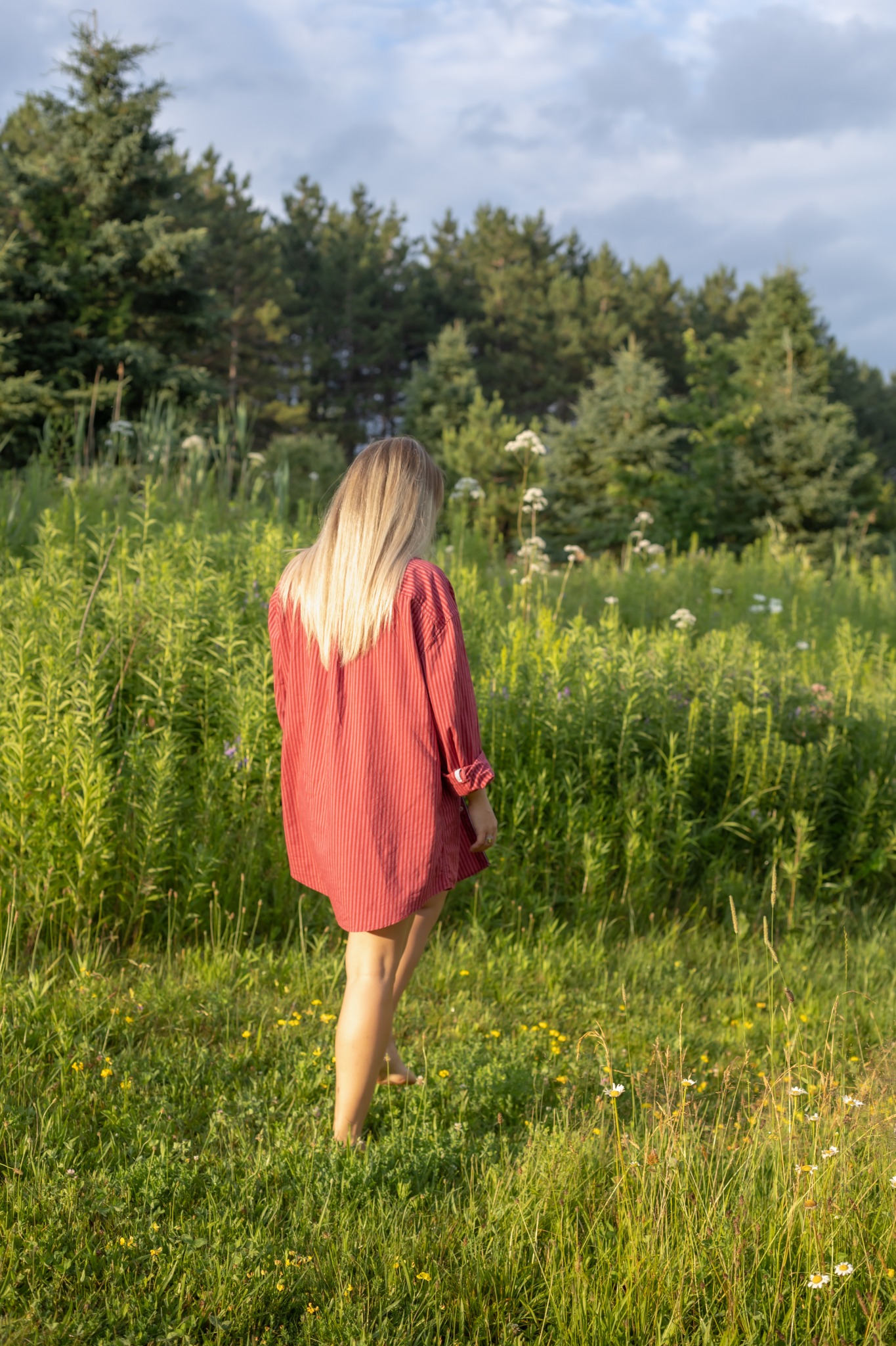 A woman walking through a sunlit field, back turned